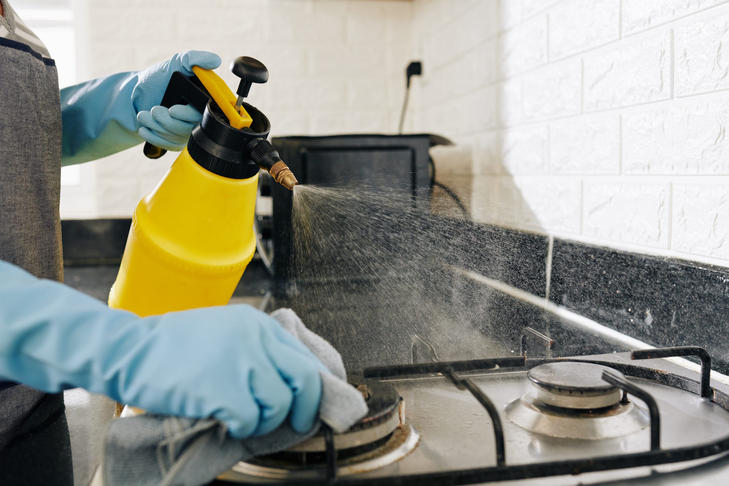 Close-up image of housewife spraying kitchen stove with deteregent to dissolve grease stains